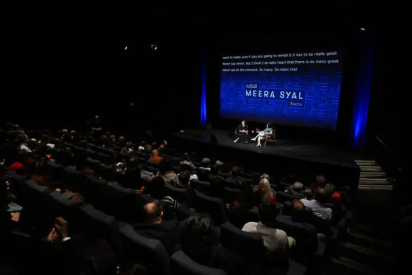 A dark cinema with people watching two women talk on stage.