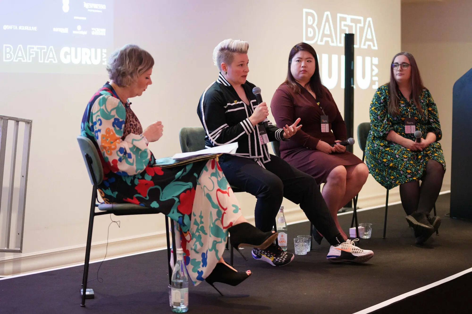 Four women sat on a stage having a discussion while holding microphones.