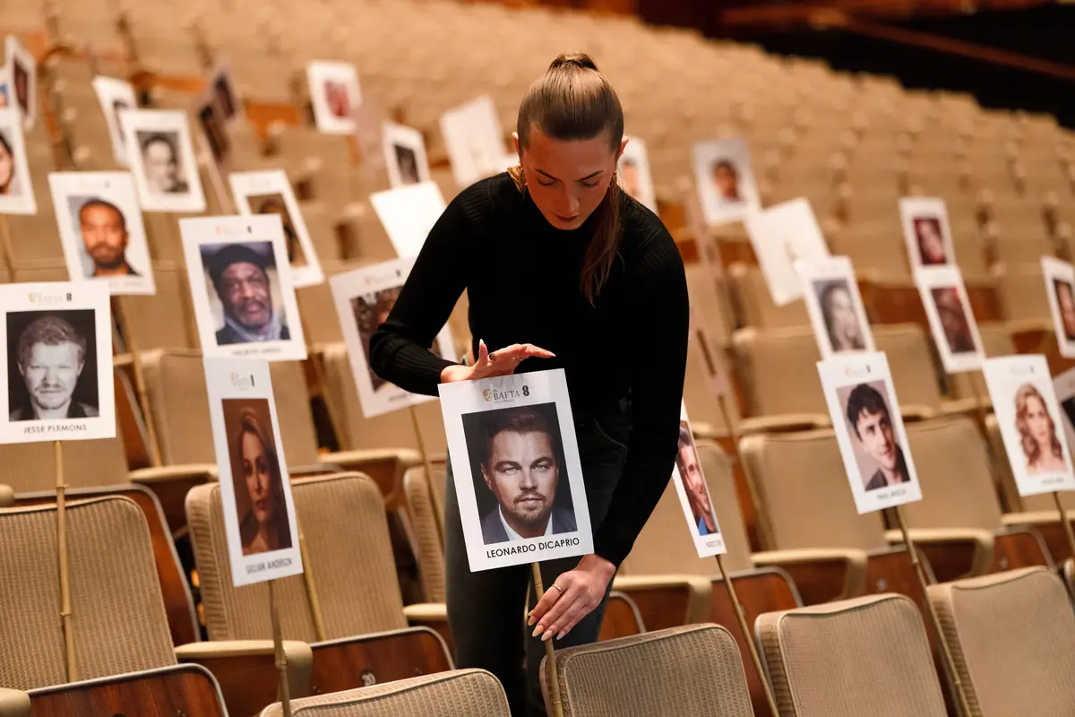 A woman can be seen in a theatre setting, placing headshots of film stars for a photo call 